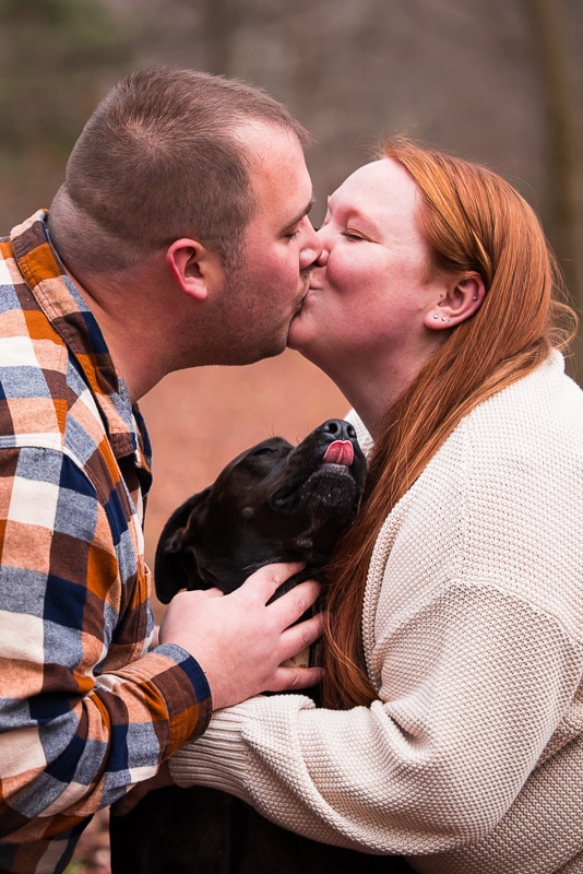 Creative Engagement Photographer, lisa rhinehart, captures the couple kissing with their dog looking up at them with its tongue out during their central pa engagement session
