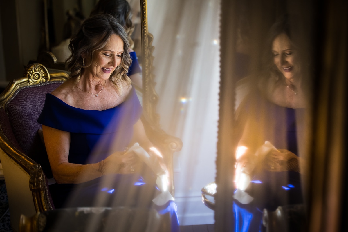 unique, creative image of the bride's mom opening a gift as her reaction is also captured in the mirror before this Ashcombe Mansion wedding 