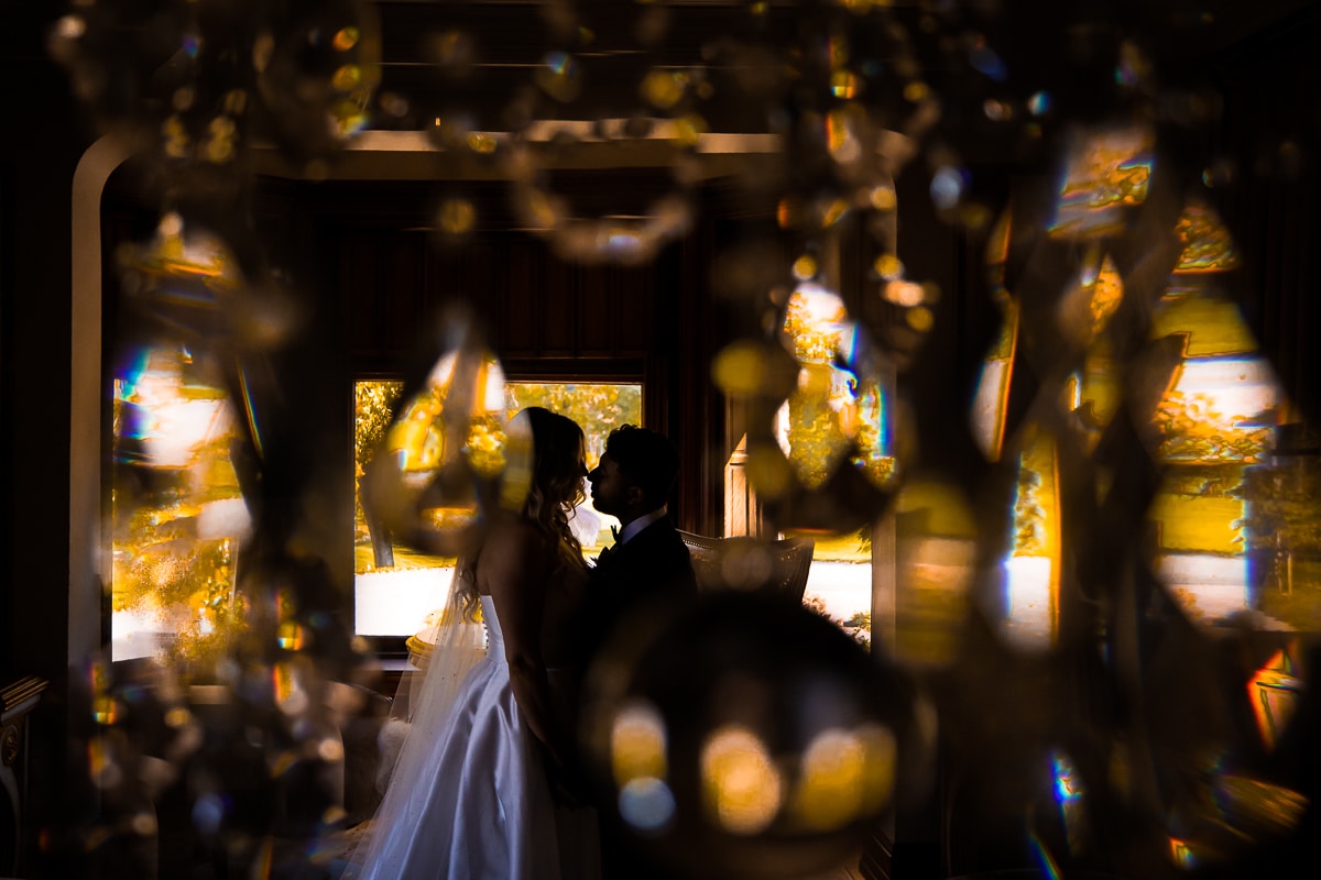 unique, creative image of the bride and groom almost kissing through a series of diamond chandelier pieces outside of the Willows of Ashcombe mansion 