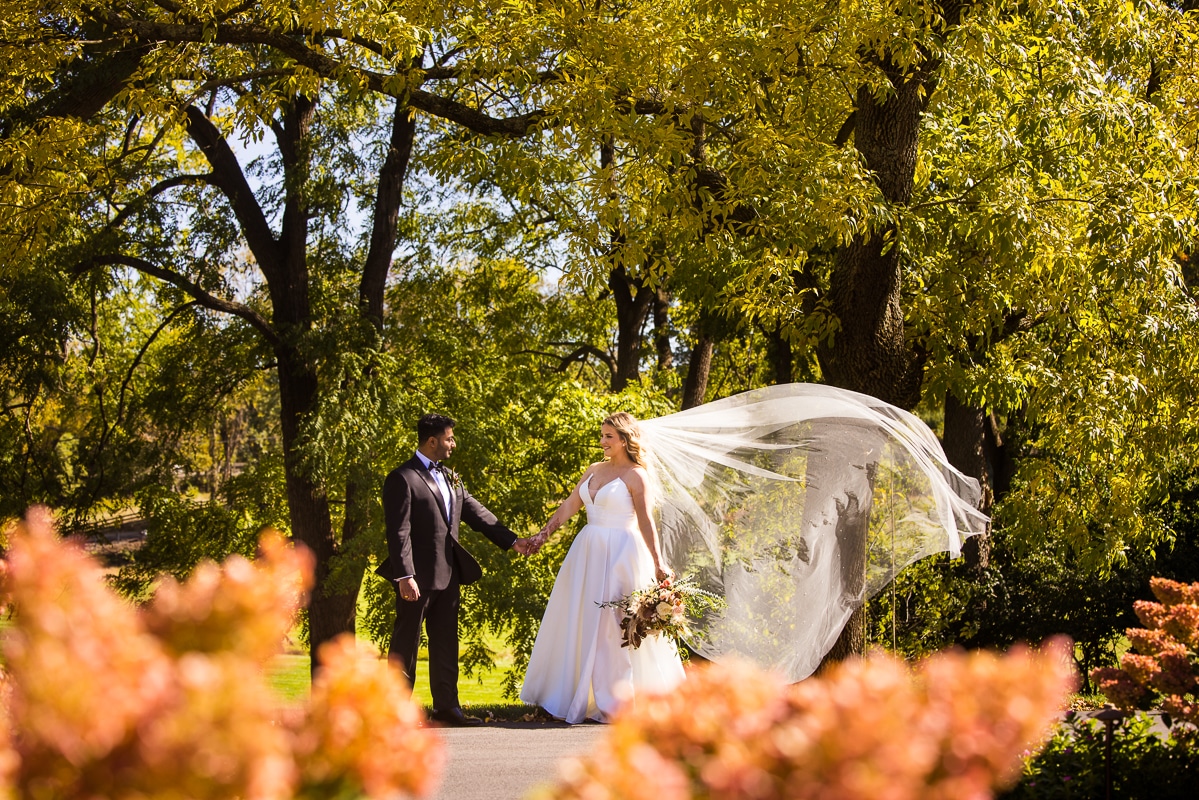 Ashcombe Mansion wedding photographer, lisa rhinehart, captures the bride and groom standing outside holding hands as her veil blows in the wind before their wedding ceremony in mechanicsburg, pa 