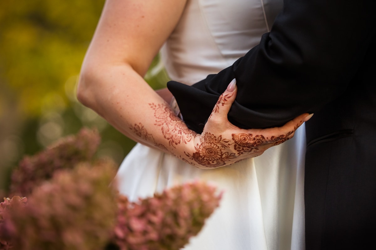 Creative wedding photographer captures a close up of the bride's henna decorated hand and her nails as she wraps her hand around the groom's arm 