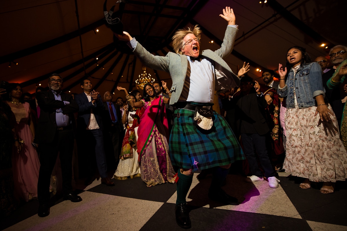 wedding photographer, lisa rhinehart, captures a guest dress in a kilt dancing and singing in the middle of the dance floor surrounded by other guests during this mansion wedding reception 
