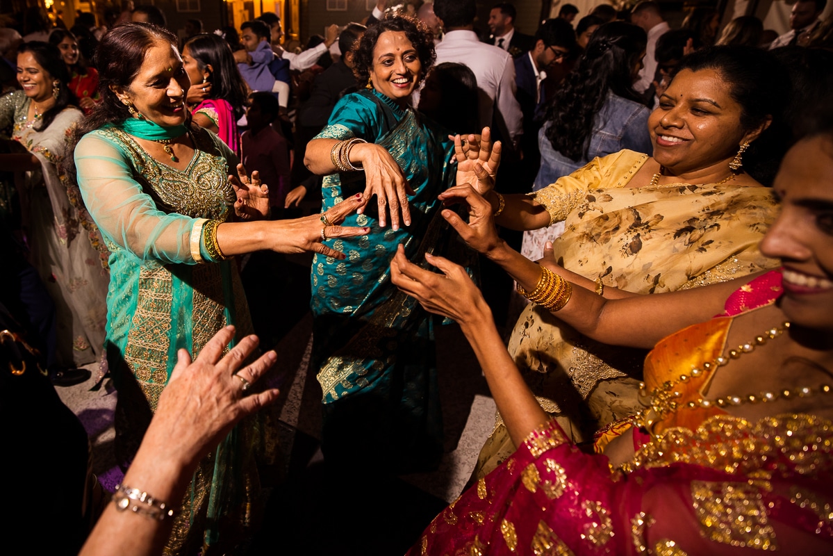 colorful image of guests dressed in green, blue, yellow, pink, purple, traditional indian wedding attire dancing around during this ashcombe mansion reception 