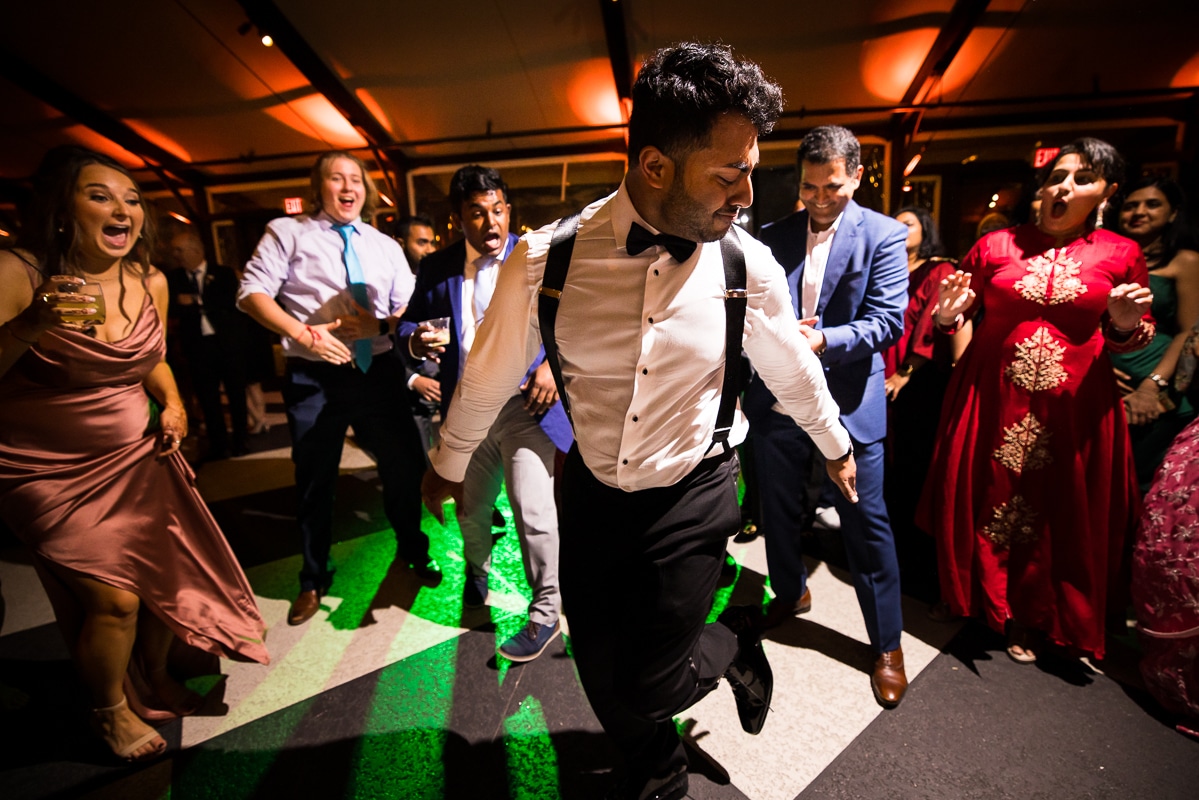 image of the groom dancing as guest stand around cheering for him with green lights reflecting on the floor of the mansion during their wedding reception in mechanicsburg pa 
