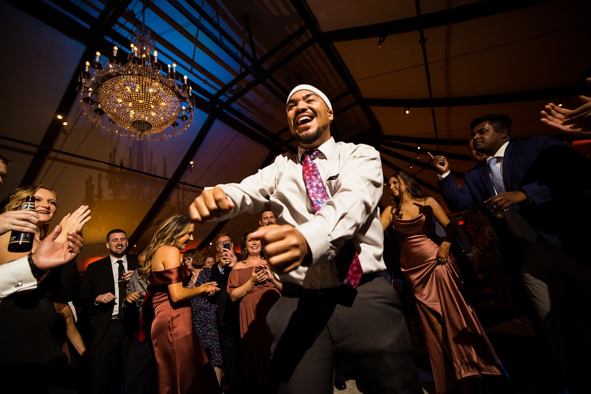best pa wedding photographer captures a guest with a purple and pink tie dancing around as guests dance behind him during this mechanicsburg wedding reception 