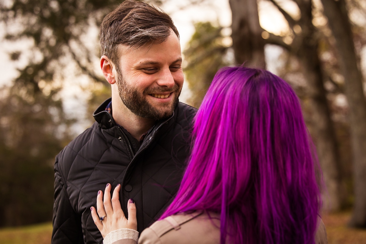 Image of the couple smiling at one another with the focus on the future husband smiling as his fiance as she looks at him during their engagement session at Murray Hill
