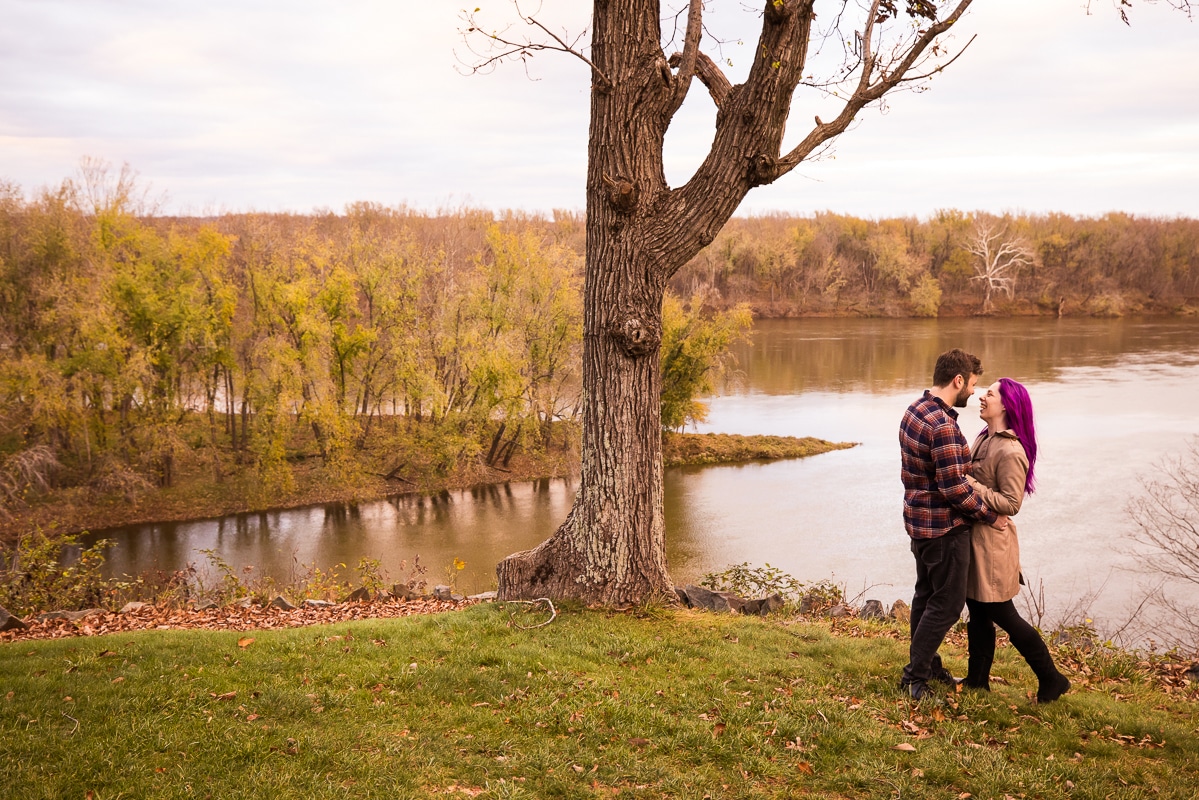 Image of the couple hugging one another and smiling at each other with a the Potomac River in the background of their engagement session at Murray Hill, Virginia