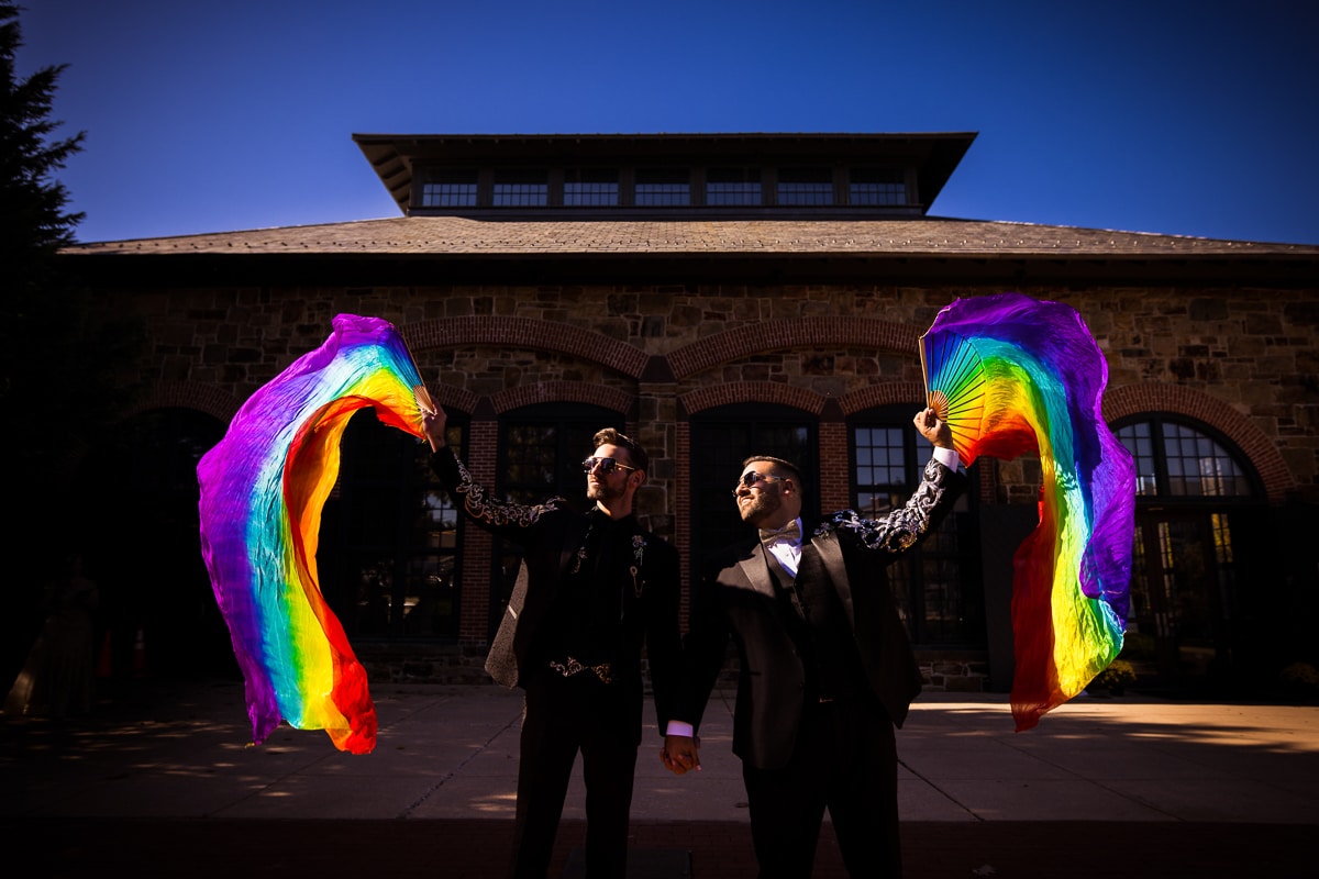 LGBT Wedding Photographer, Lisa Rhinehart, captures this image of this gay couple flying rainbow flags through the air during their Phoenixville Foundry wedding