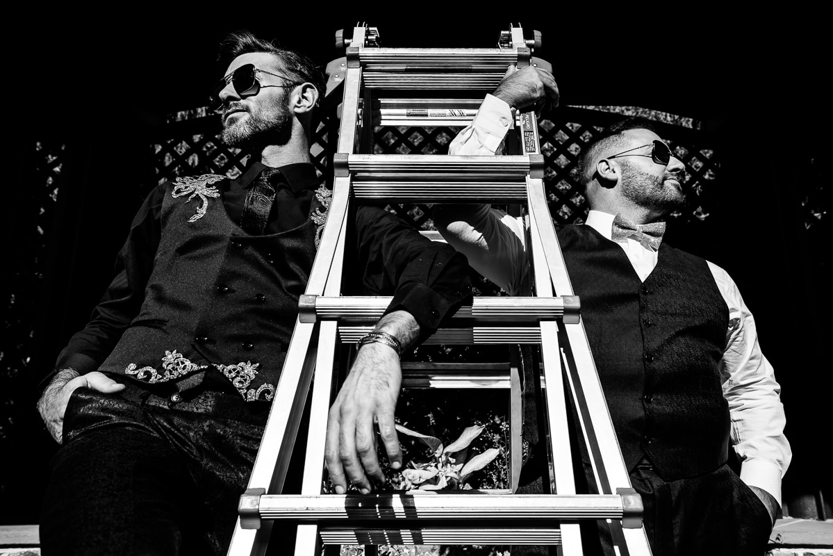 Philadelphia wedding photographer, Lisa Rhinehart, captures this black and white image of this gay couple posing with a ladder and their sunglasses before their wedding ceremony