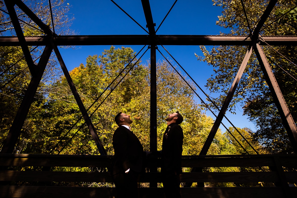 Best PA Wedding Photographer, Lisa Rhinehart, captures this creative image of the couple on a bridge looking up towards the bright blue sky before their fall wedding in Philly