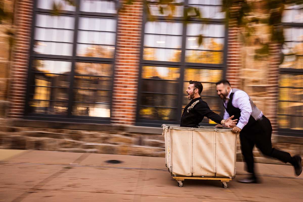 Lisa Rhinehart, pa wedding photographer, captures this motion blur image of one of the grooms inside a laundry cart as the other one pushes him in it outside of the Phoenixville Foundry in Philadelphia, PA