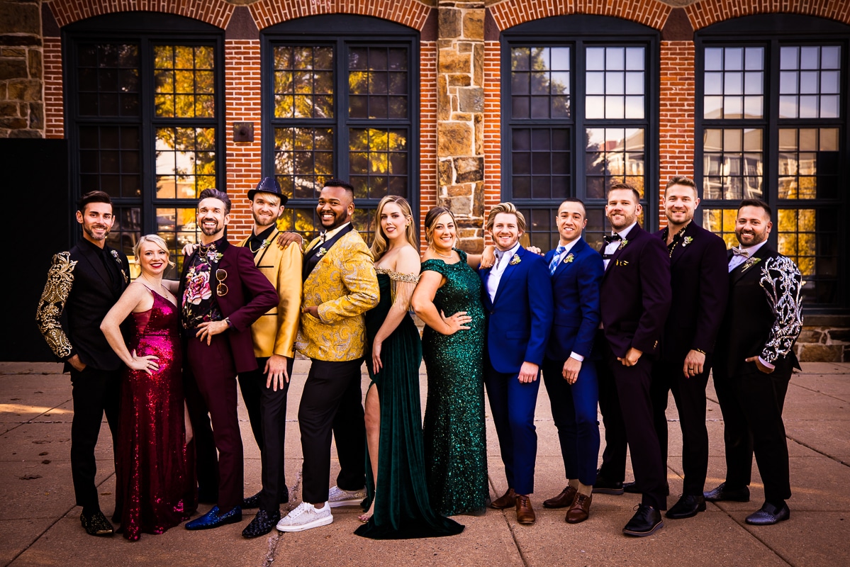 Traditional portrait of the wedding party in a rainbow line in their jewel toned attire before this gay wedding at the Phoenixville foundry in Philadelphia, pa
