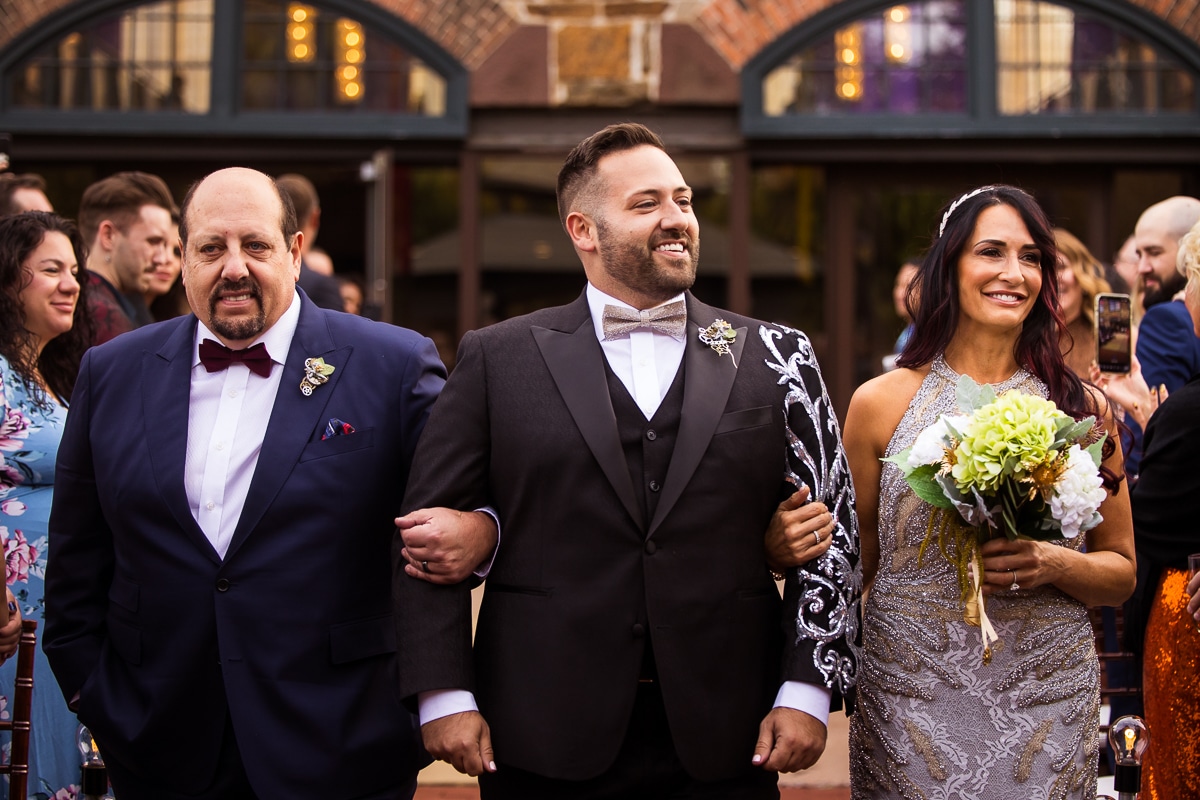 image of the groom walking down the aisle with his mom and dad during the wedding ceremony at the Phoenixville foundry 