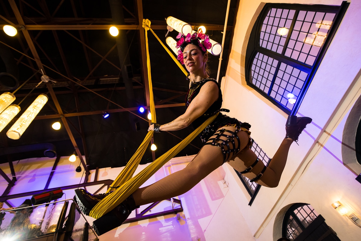 LGBT Wedding Photographer, Lisa Rhinehart, captures this image of an aerialist hanging from the ceilings during this couple's cocktail hour at their Phoenixville Foundry wedding