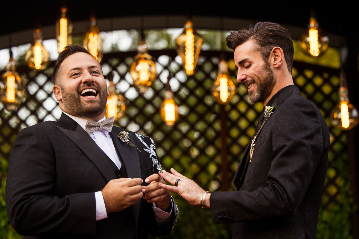 image of the groom smiling down at his new ring as the other groom smiles out towards their wedding guests during their Phoenixville foundry wedding ceremony 