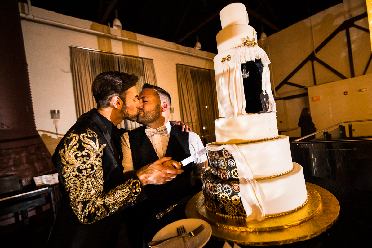 image of the husbands kissing as they cut their cake at the Phoenixville foundry in Philly, pa 