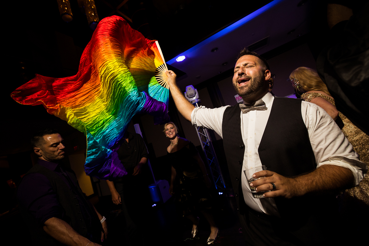 image of the groom dancing with a rainbow flag in his hand and a drink in his other hand during this gay wedding reception in philly