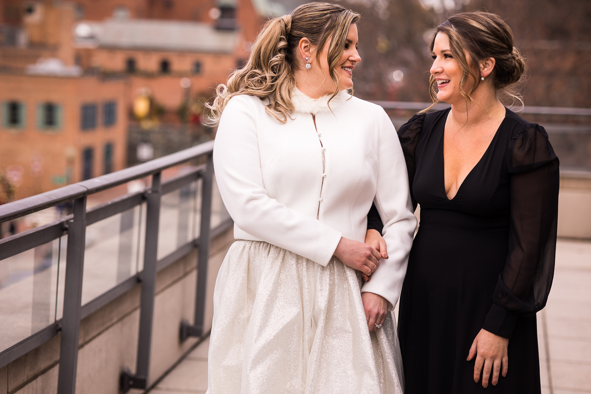 Candid image taken by DC wedding photographers, rhinehart photography, of the bride and her sister walking arm and arm laughing and smiling at one another as they walk across the balcony outside of the hotel before the wedding ceremony 