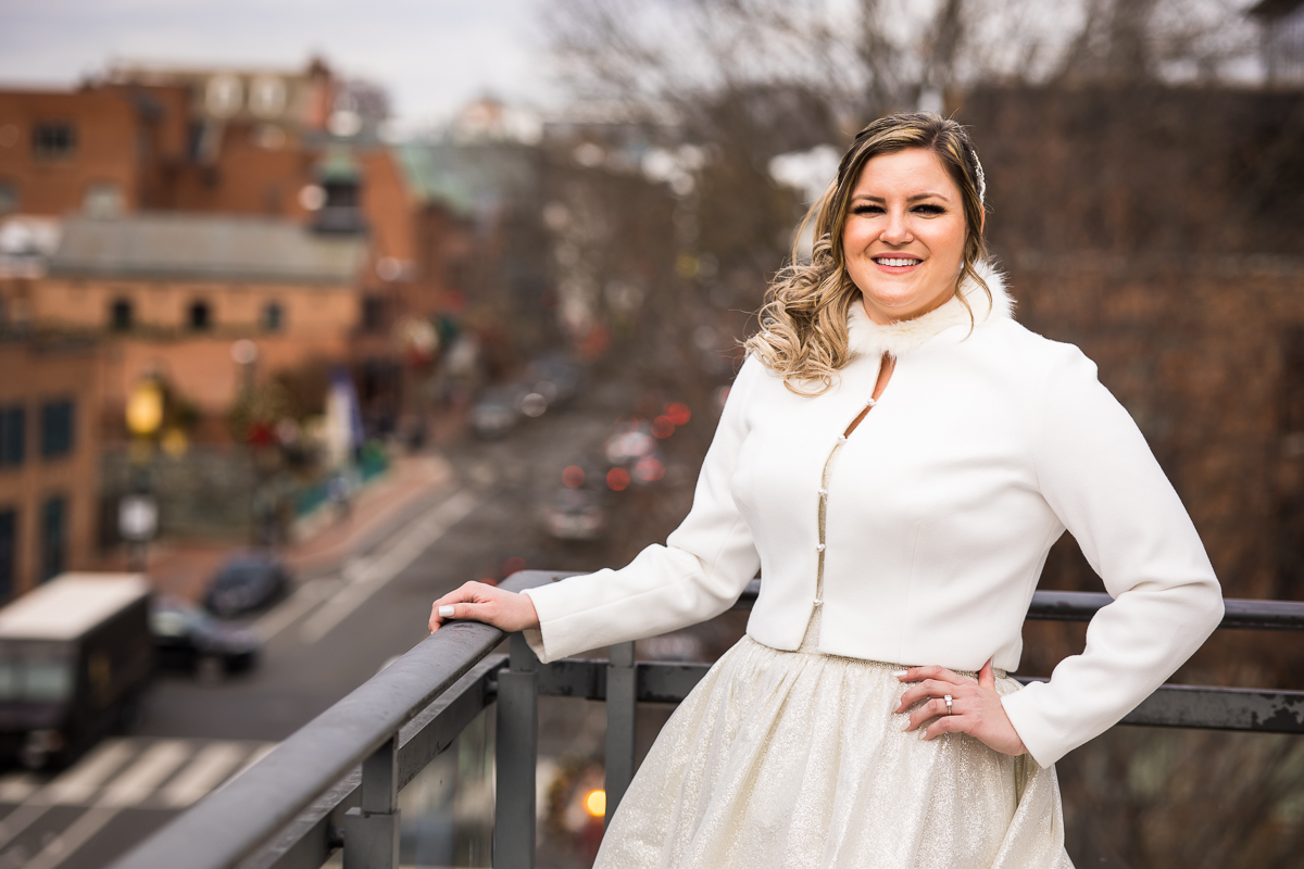 Traditional portrait of the bride standing alone with her hand on her hip and other hand on the balcony as she smiles at the camera with the busy city blurred behind her before her wedding ceremony at the ritz carlton