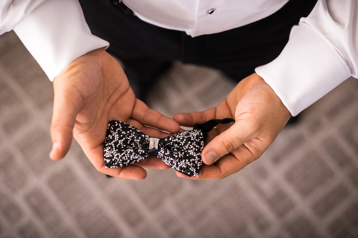 Image of the groom holding his unique and non traditional sparkly black and silver bow tie in his hands as he is getting ready before their wedding ceremony in DC
