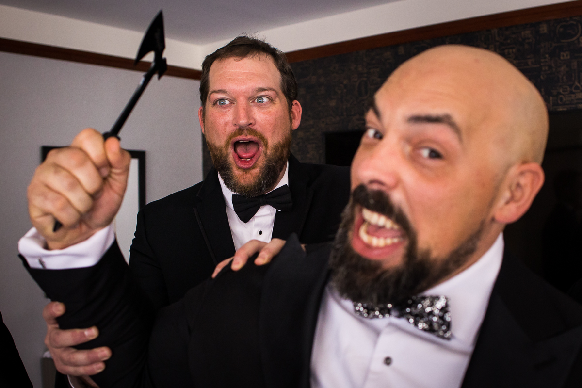 Creative, unique image of the groom loooking at the camera holding up his axe as one of his groomsmen standing behind him trying to hold him back from hitting the camera during their preparations before their Georgetown wedding 