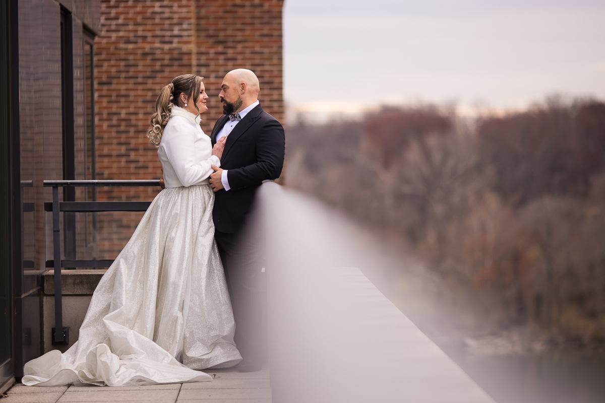 Ritz Carlton Georgetown Wedding photographers, rhinehart photography, captures this creative, unique perspective of the couple close hugging one another with the winter scenery behind them and the railing of the balcony as a blurred line leading to the couple during their Washington dc wedding 