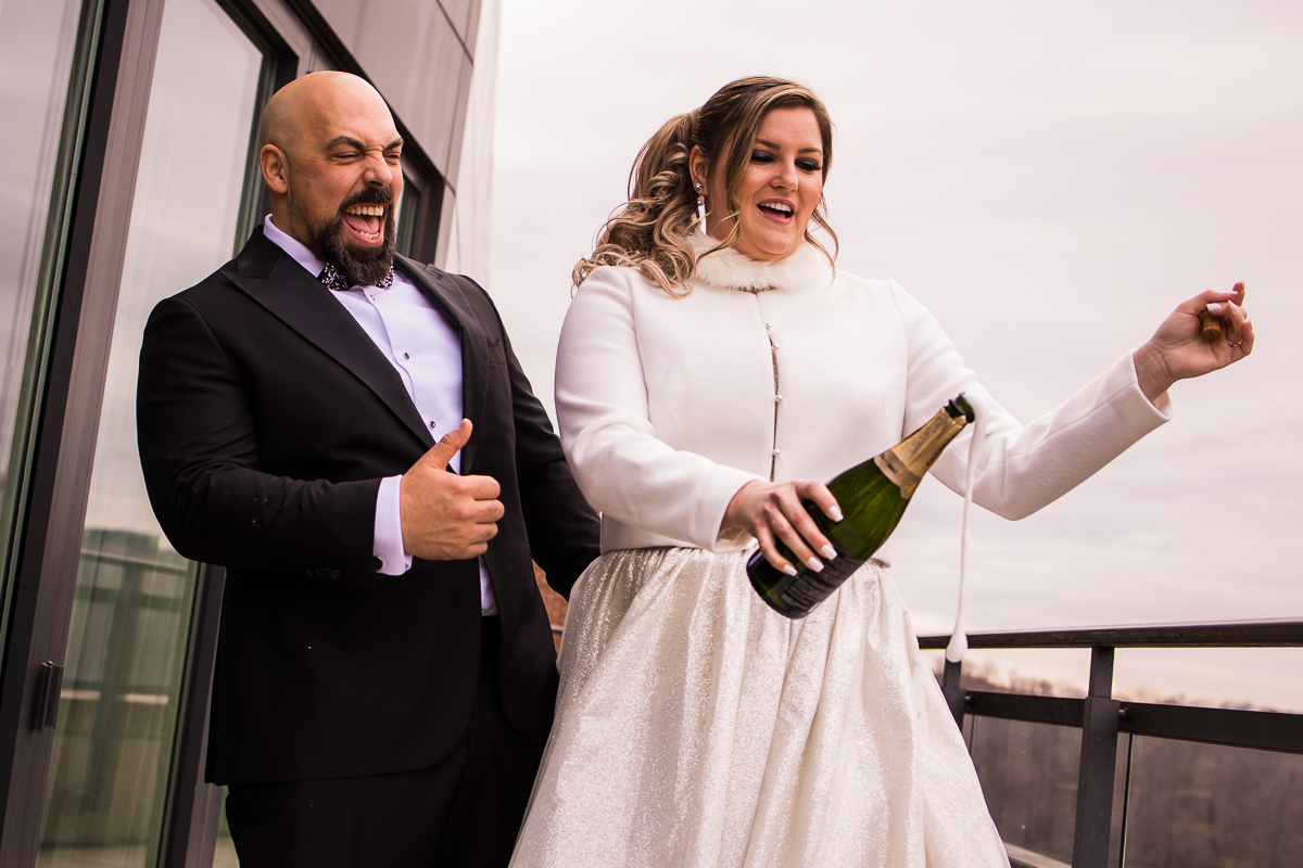 Candid image of the bride and groom laughing and smiling as they pop the champagne bottle outside of the ritz carlton hotel 
