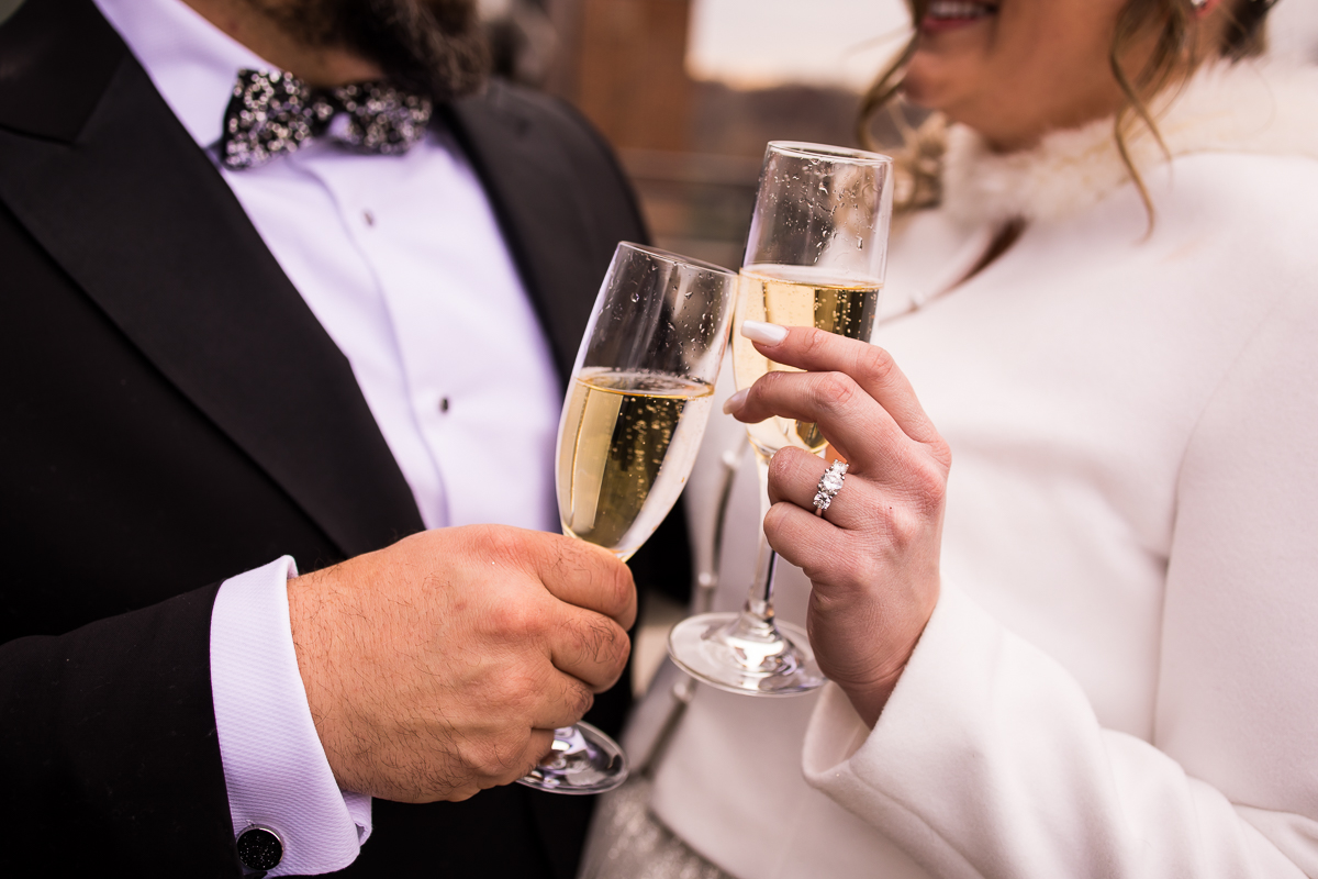 Unique, close up image of the bride and groom holding champagne classes and clink them together as you can see the grooms sparkly bowtie and the brides sparkly ring 
