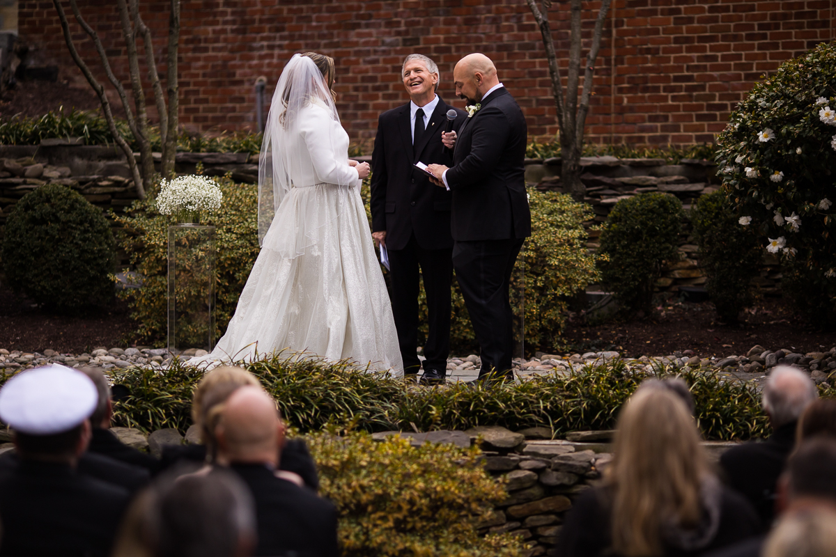 Image of the bride and the groom saying their vows as the officiant laughs as the groom says his vows during their outdoor winter wedding ceremony 