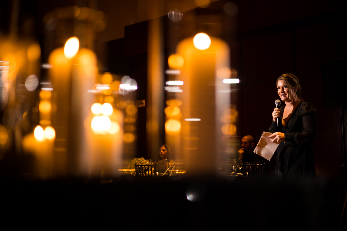 creative, unique image of the sister giving her speech during the wedding reception with reflections of blurred candles in front of her 