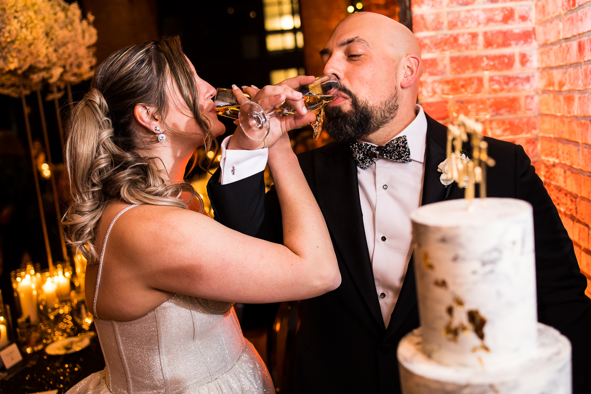 image of the bride and groom drinking their champagne glasses behind of their wedding cake 