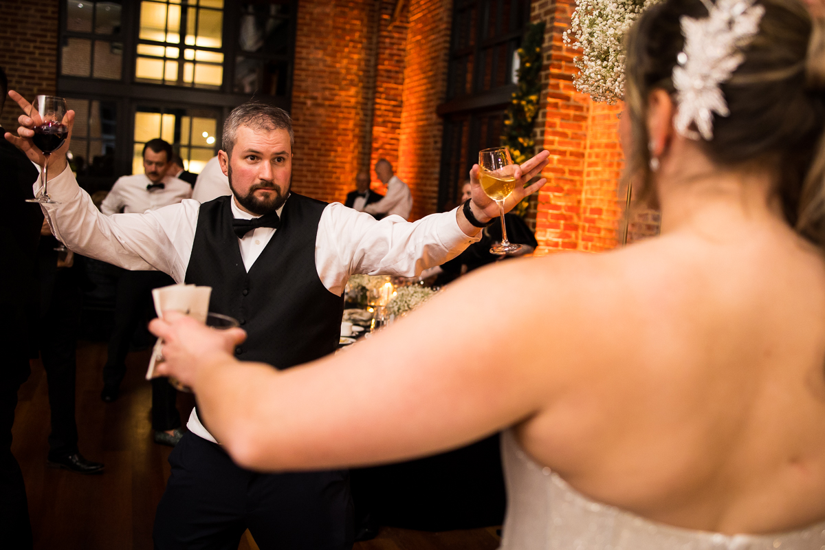 image of a guest with drinks in both hands as he walks to the bride during this indoor wedding reception 