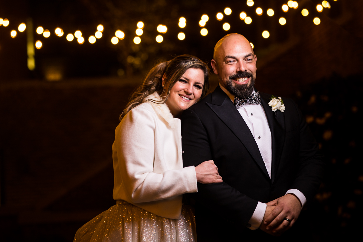Ritz Carlton Georgetown Wedding photographers, rhinehart photography, captures this end of the night image of the couple hugging and smiling at the camera with twinkle lights blurred behind them 