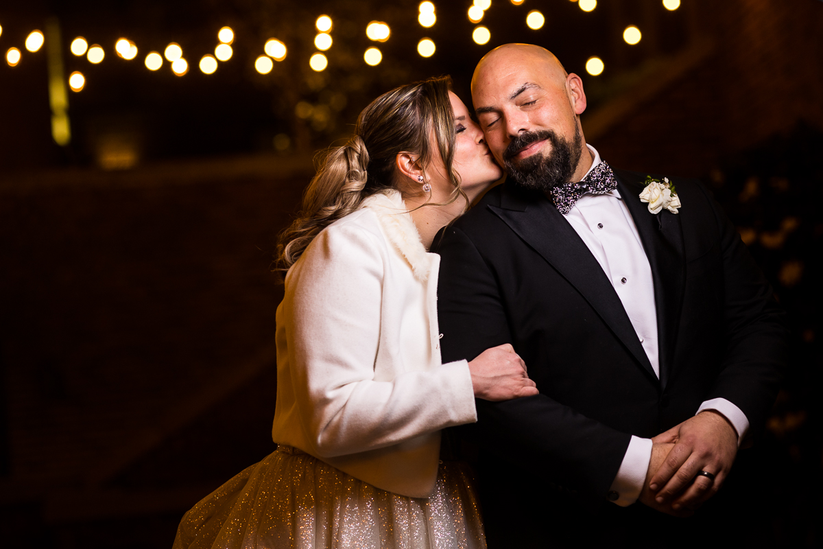 Ritz Carlton Georgetown Wedding photographers, rhinehart photography, captures this end of the night image of the couple hugging and smiling and kissing with twinkle lights blurred behind them 