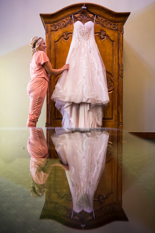 unique, creative wedding photographer, lisa rhinehart captures this image of the bride looking at her dress and smiling as she holds it and the reflection of her and her dress are captured on the bottom of the image