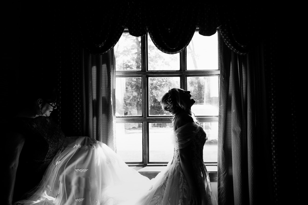 Pocono Wedding Photographer, lisa rhinehart, captures the brides silhouette in the window as she is laughing before her wedding ceremony and first look at the stroudsmoor woodsgate wedding ceremony