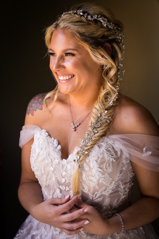 Wedding photographer, lisa rhinehart, captures the bride all dressed and ready with silver gems wrapped into her braid as she smiles out the window before her stroudsmoor wedding ceremony