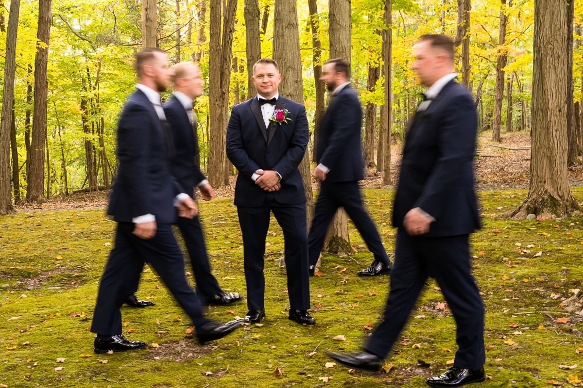 Creative Pocono Wedding Photographer, lisa rhinehart, captures the groom looking towards the camera with his hands crossed as his groomsmen are motion blurred as they walk around him 