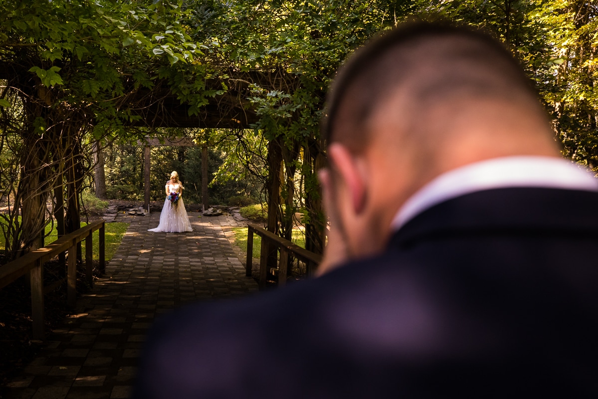 Unique image of the bride standing at one end of the bridge as the groom stands at the other before their first look at their stroudsmoor wedding 
