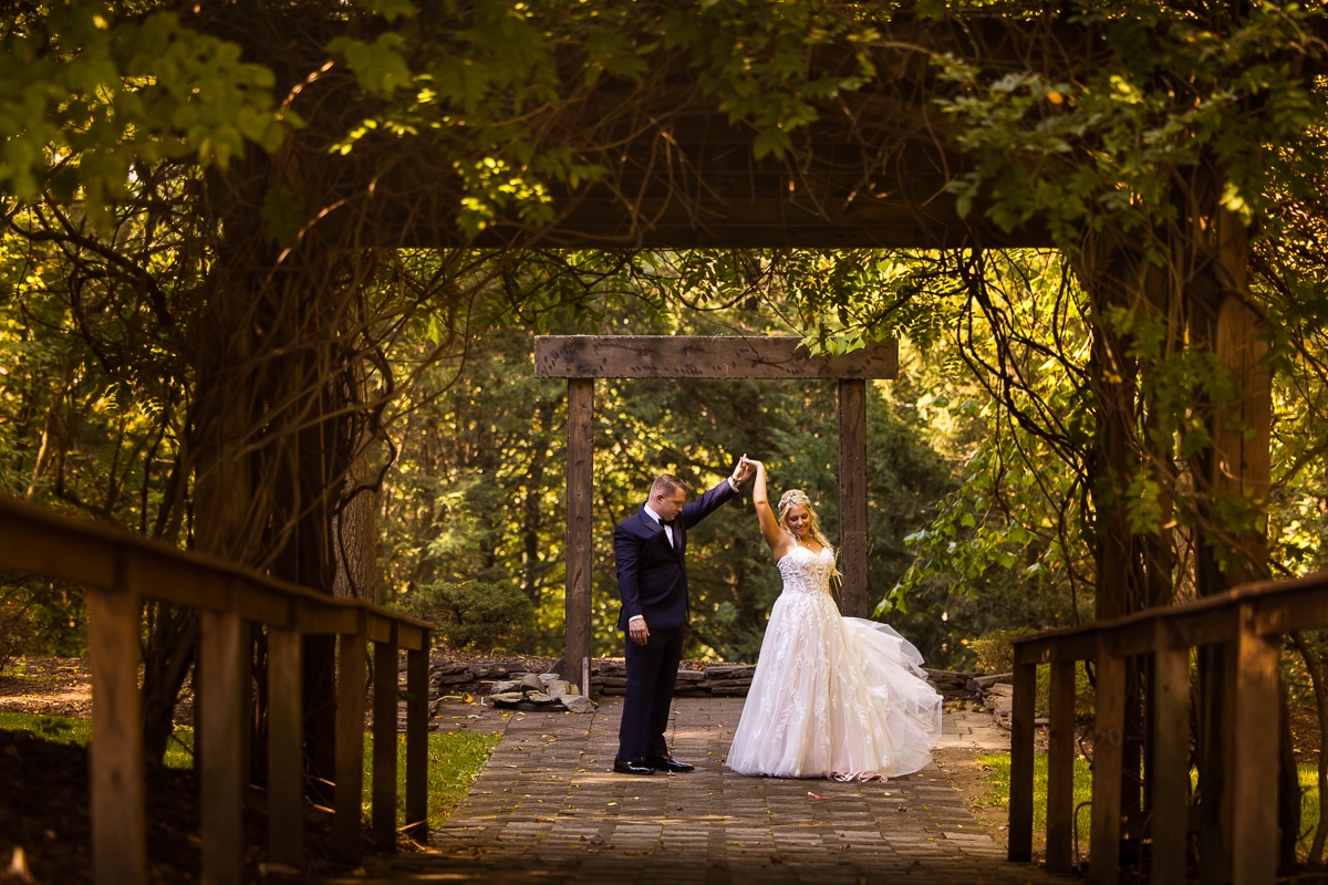 Pocono Wedding Photographer, rhinehart photography, captures the groom spinning the bride around as they are surrounded by the outdoors, and are framed in the picture by a vine covered wooden arch way at their Stroudsmoor wedding venue 