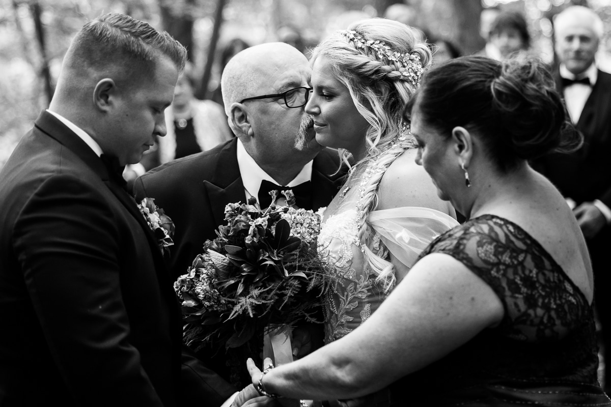 Pocono wedding photographer, lisa rhinehart, captures this black and white image of the father of the bride kissing her as they reach the end of the aisle to hand her off to the groom 