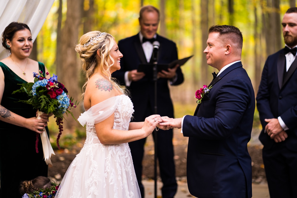 Vibrant image of the bride as she puts the ring on the groom's hand surrounded by nature and the vibrant, colorful fall leaves