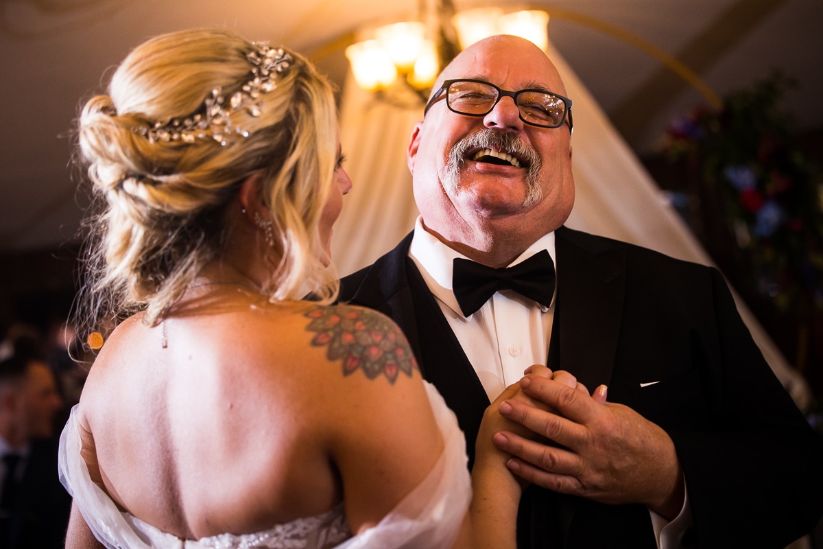 image of the bride dancing with her father as he holds her hand and is laughing and smiling while dancing together during the wedding reception in the poconos