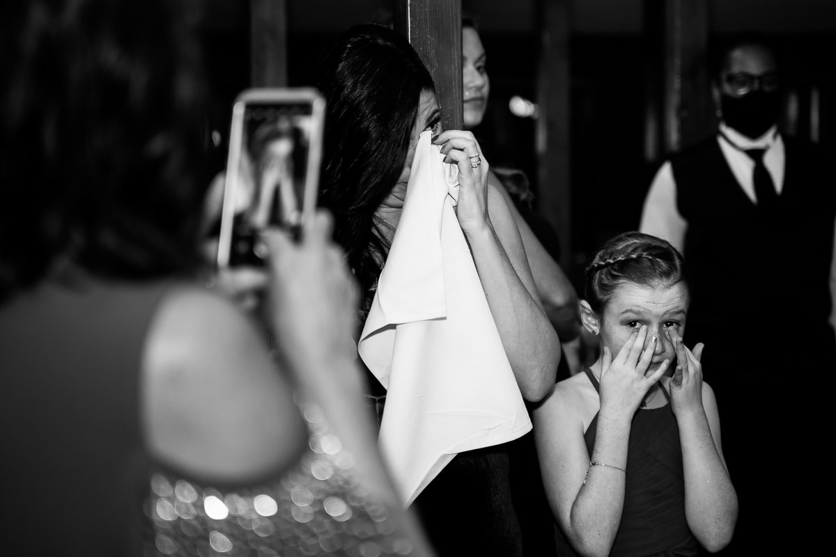 black and white image of guests wiping away tears and another guest taking a photo of it as the couple dances together during their wedding reception inside of the stroudsmoor