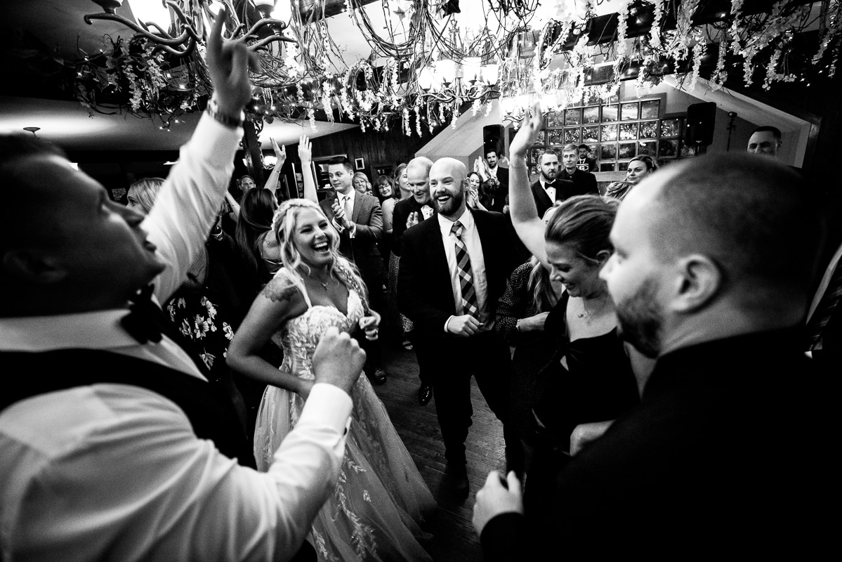 black and white image the couple and their guests dancing with huge chandeliers above their heads during their wedding reception in the poconos
