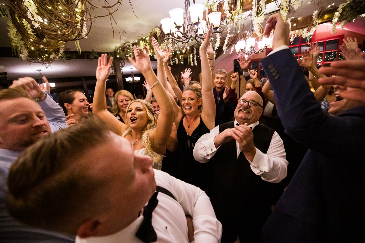 Pocono wedding photographer, lisa rhinehart, captures the couple dancing with their guests with their hands in the air during the wedding reception at the stroudsmoor as the lights and decor fill the ceiling above them 