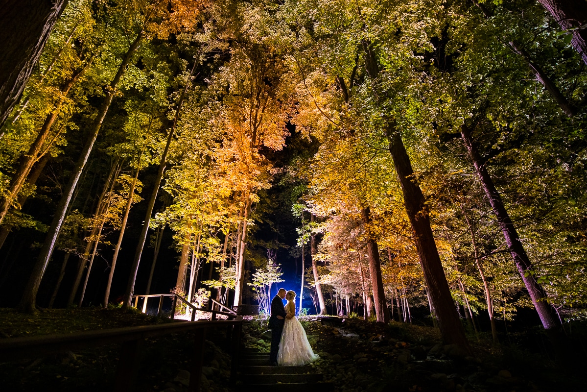 Pocono Wedding Photographer, lisa rhinehart, captures the bride and groom at night surrounded by green, orange, and yellow fall leaves on trees after their wedding at the Stroudsmoor County Inn