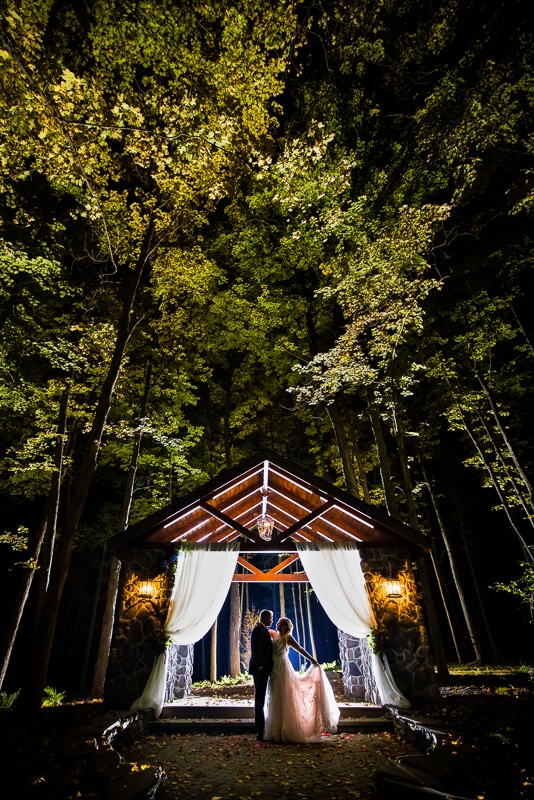 unique, creative close up image of the couple standing underneath the ceremony pavilion surrounded by tall trees after their stroudsmoor wedding reception