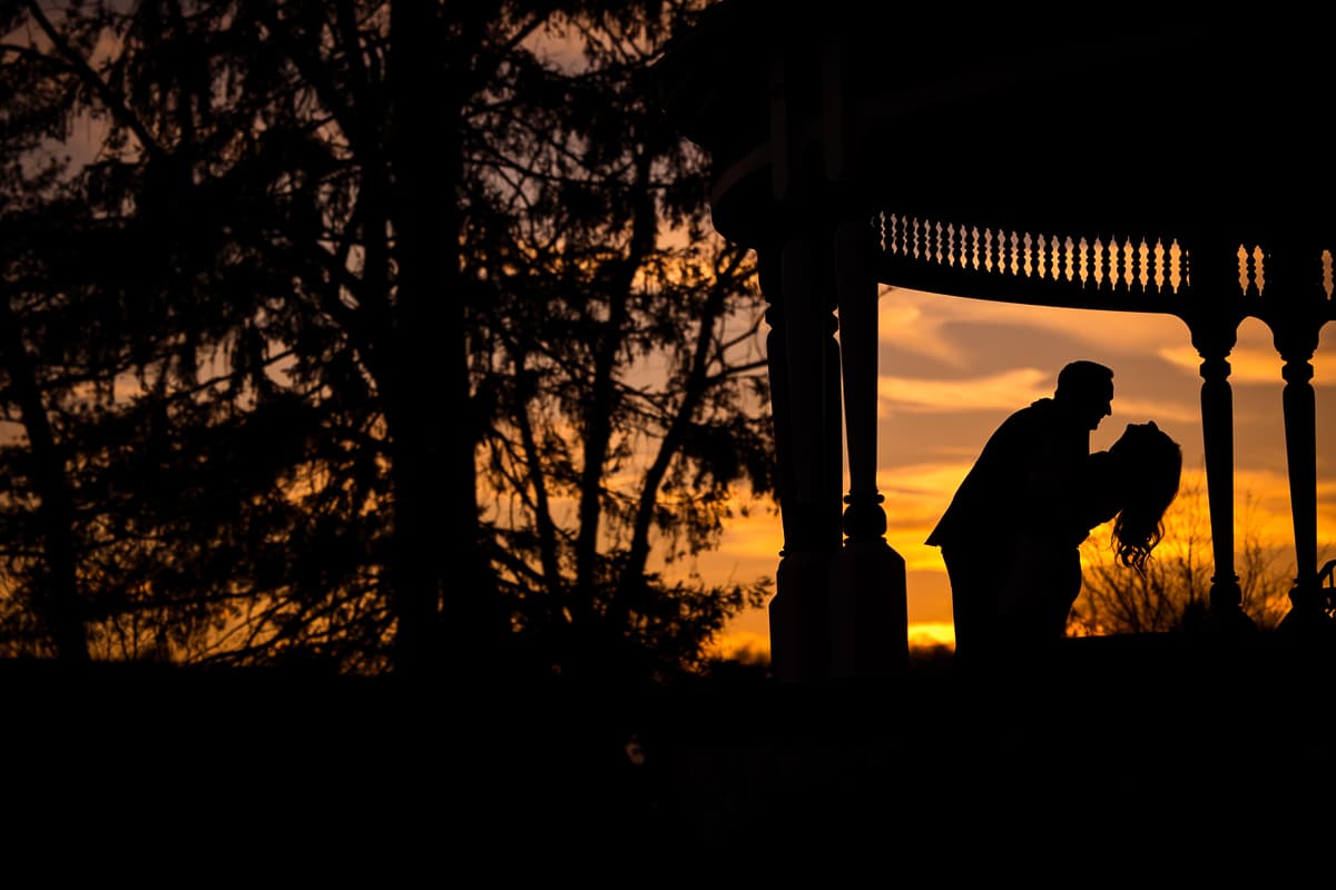 Willows at Ashcombe Mansion Engagement photographer, Lisa Rhinehart, captures this unique, vibrant, colorful image of the couple hugging one another as they are silhouetted out on the porch during the sunset in Mechanicsburg, Pennsylvania