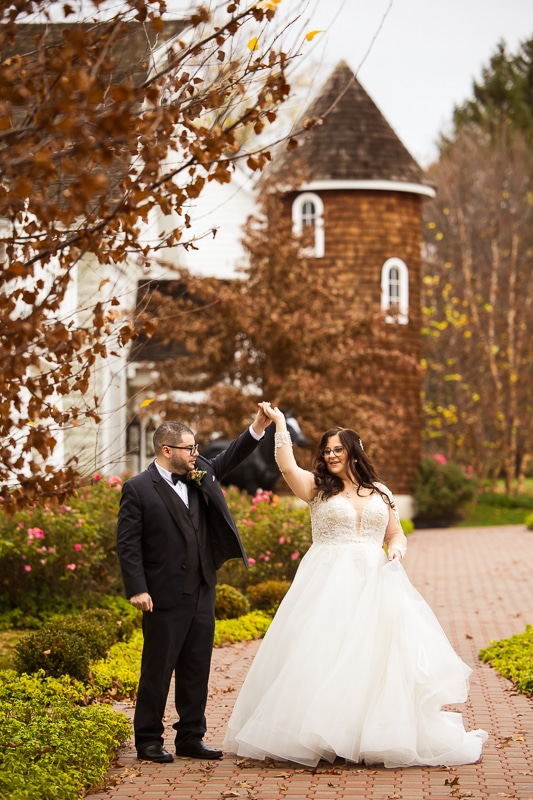 Ryland Inn Wedding Photographer, lisa rhinehart, captures the groom spinning the bride around in a circle as they stand on a brick pathway with brick buildings in the background during their fall wedding 